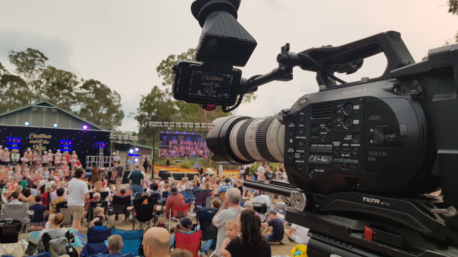 Broadcast camera facing an outdoor concert crowd