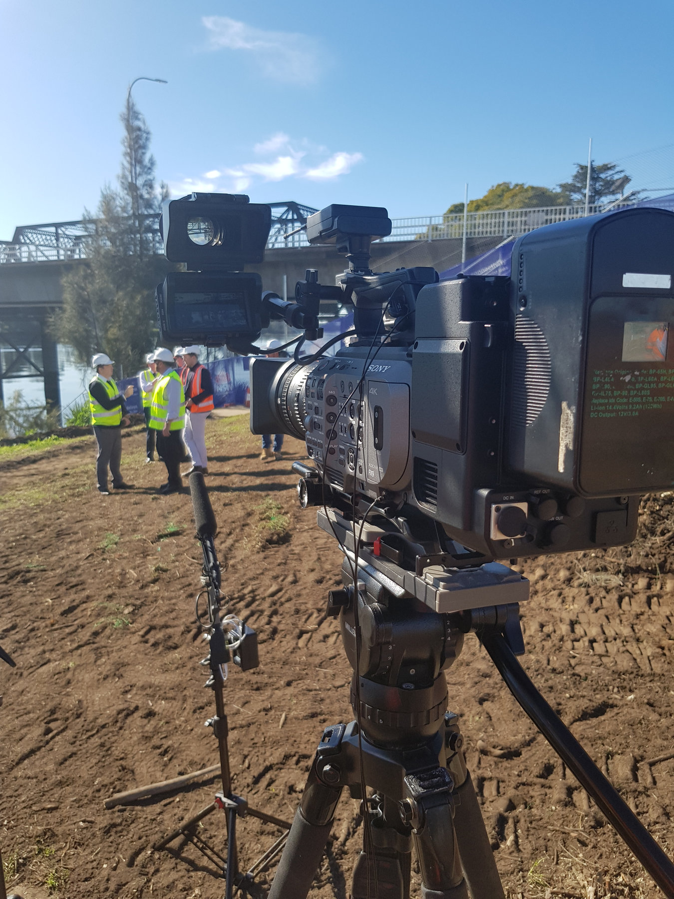 A camera on a tripod on a construction site with workers in hi-vis behind