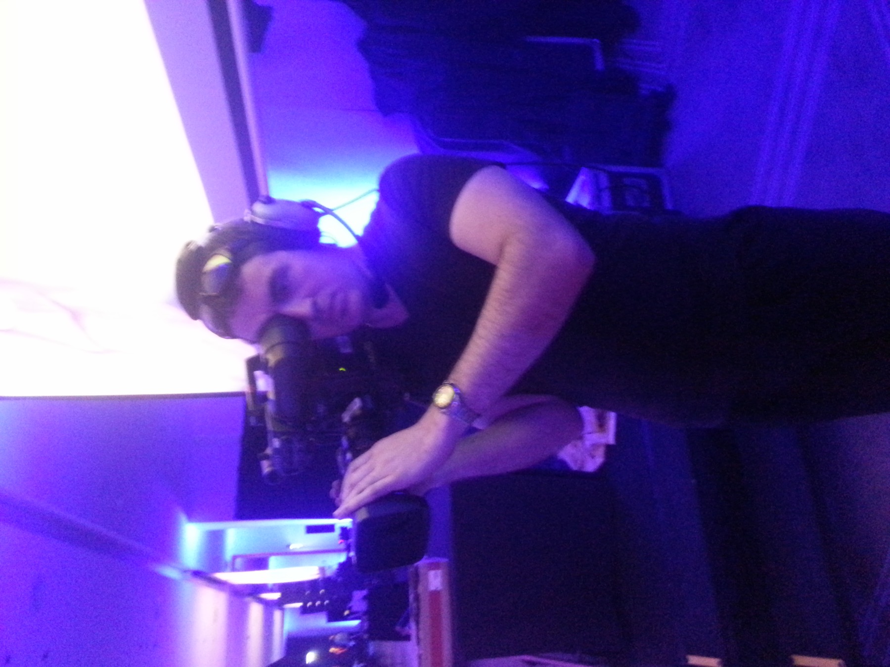Evan with a camera on his shoulder under purple event lighting