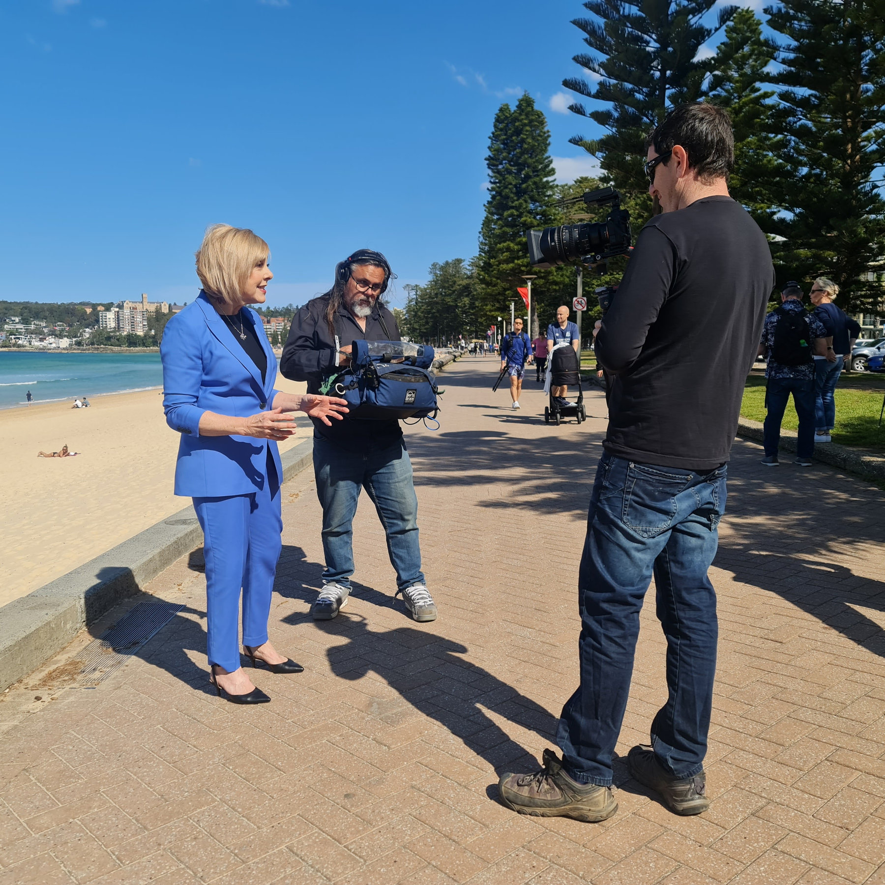 Evan filming a presenter in a blue suit with a gimbal by the beach
