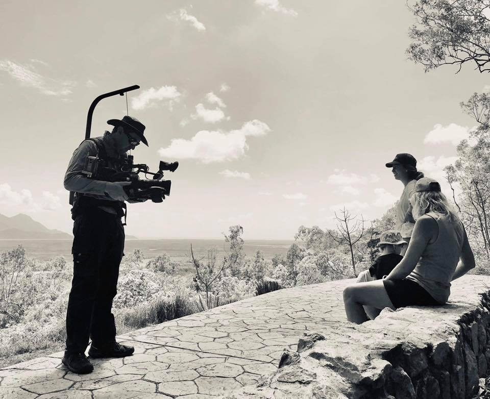 Evan Zell in an Akubra with a shoulder-mounted camera and EasyRig, filming talent on a clifftop lookout