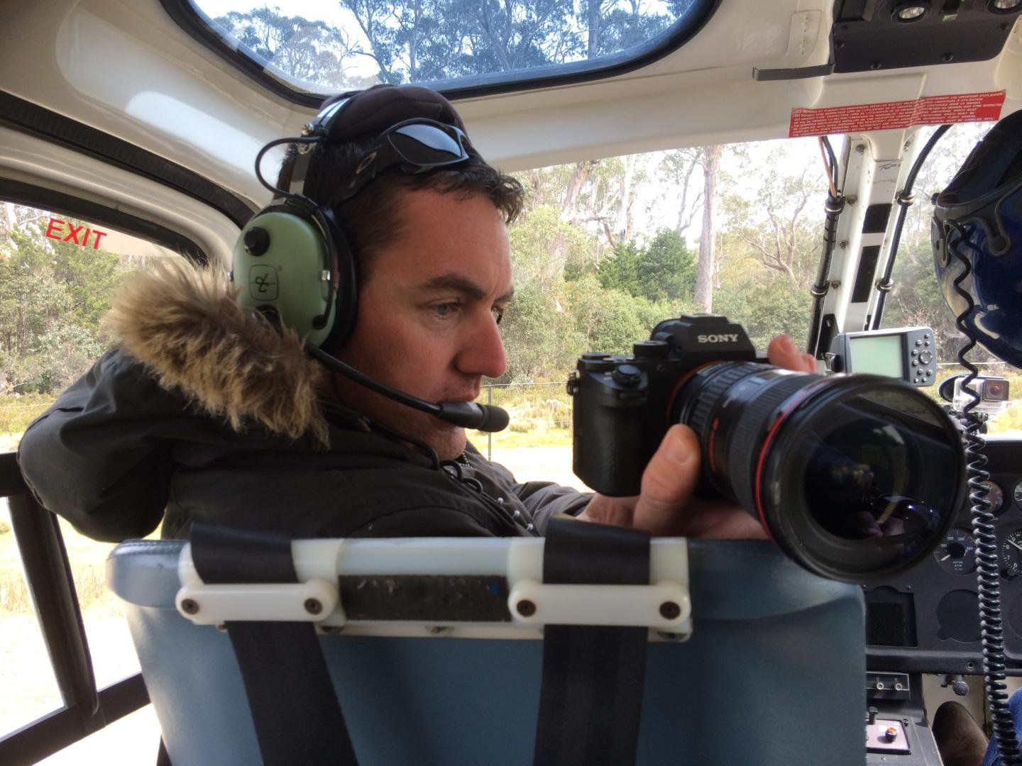 Evan Zell filming from the open door of a helicopter wearing a headset