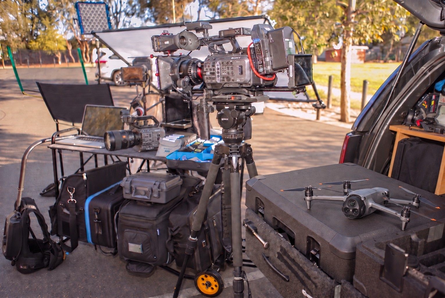 The kit laid out in a car park: Sony FX9 on the tripod, FX6 on the table, DJI Mavic 4 Pro on the case, lighting, monitors and cases