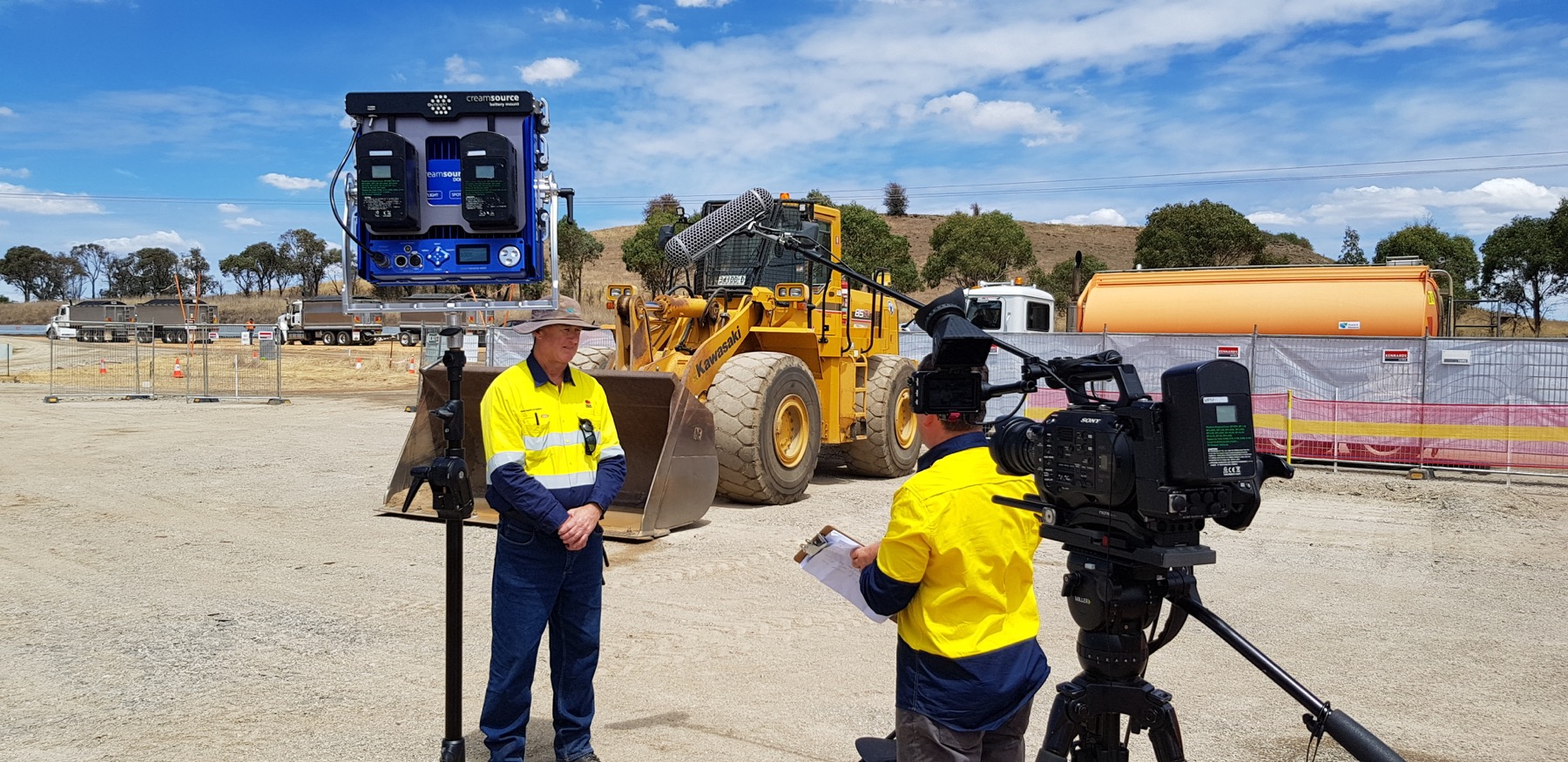 Evan filming a worker in hi-vis in front of an excavator